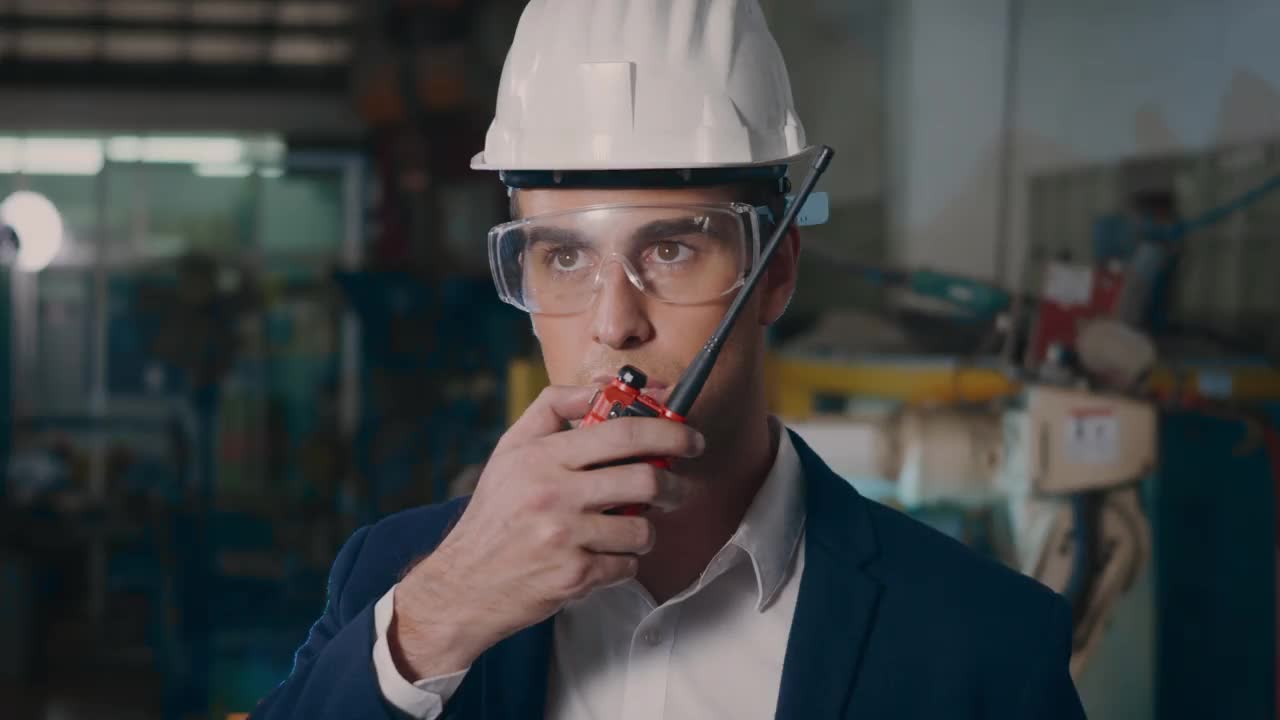 在一个重工业中，穿着西装、安全帽和护目镜的商人拿着对讲机视频下载