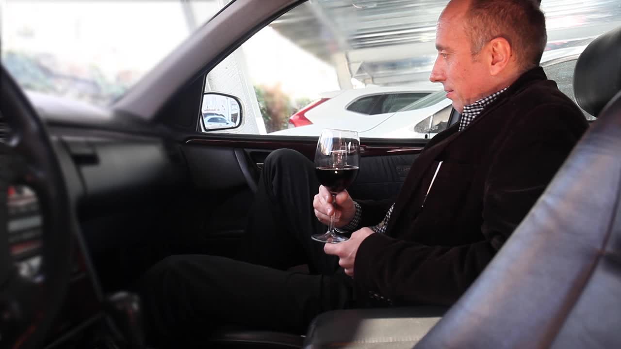 一个男人坐在车里喝了一杯红酒。视频下载