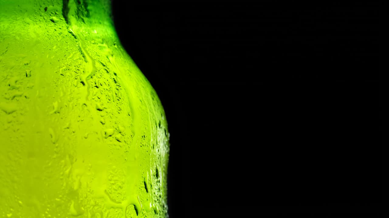 一瓶冰啤酒在黑暗的背景下慢慢旋转。视频下载