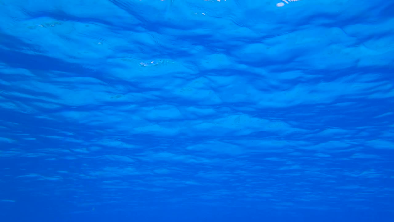 蓝色的水面上有小波浪。蓝色的海洋，水下拍摄。水下的背景视频下载