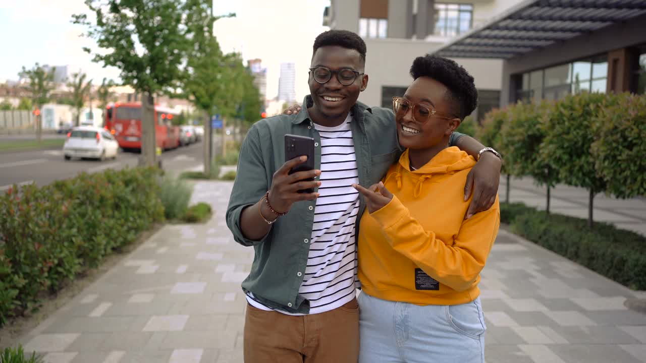 年轻夫妇走在城市里，看着智能手机，微笑着视频素材