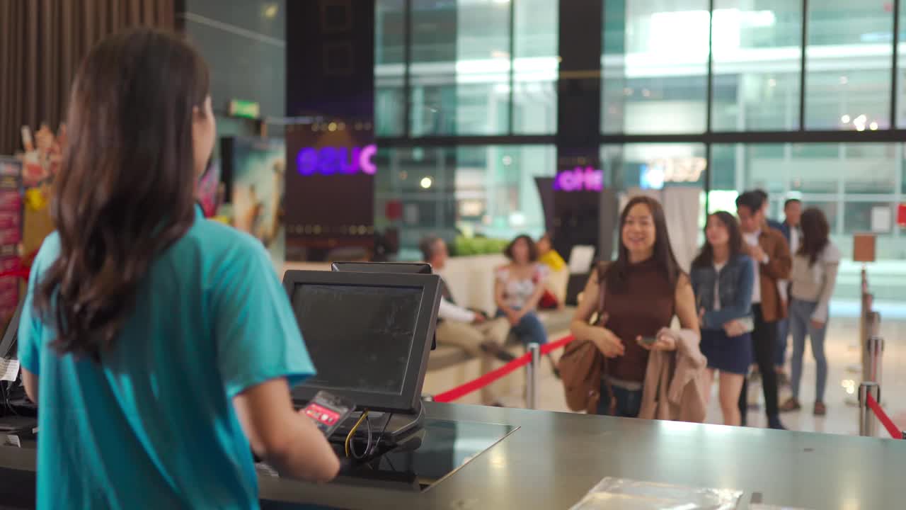 亚洲华人女性顾客在电影院售票处购买电影票，非接触式支付视频素材