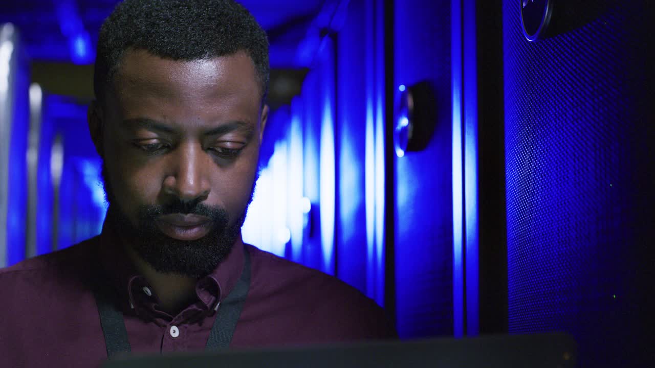 一段年轻男子在服务器室使用笔记本电脑的4k视频视频素材