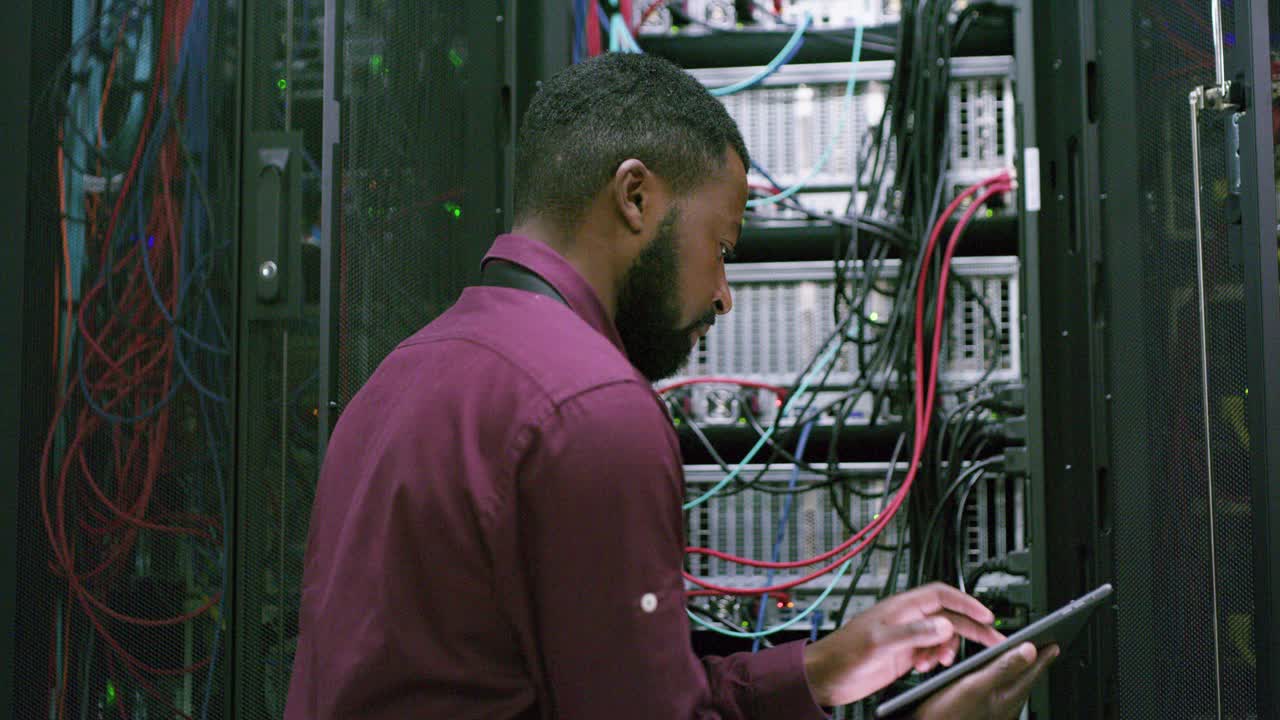 一段年轻男子在服务器室工作时使用数字平板电脑的4k视频视频素材