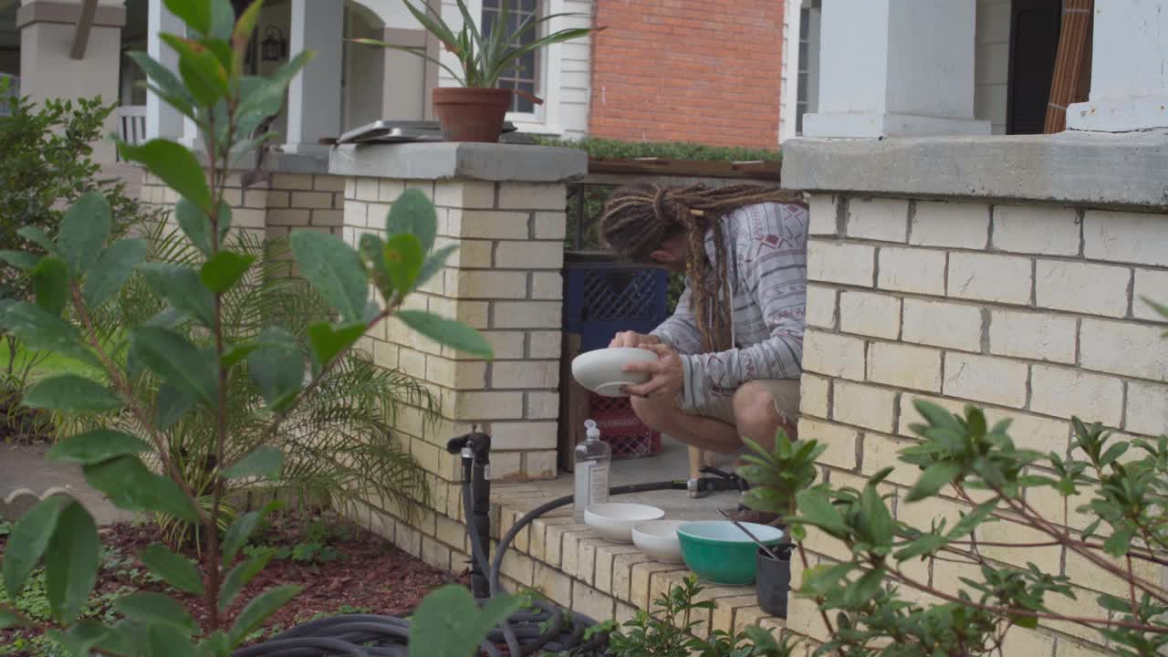 一个专注的年轻人在户外洗盘子，他的狗陪伴着他视频素材