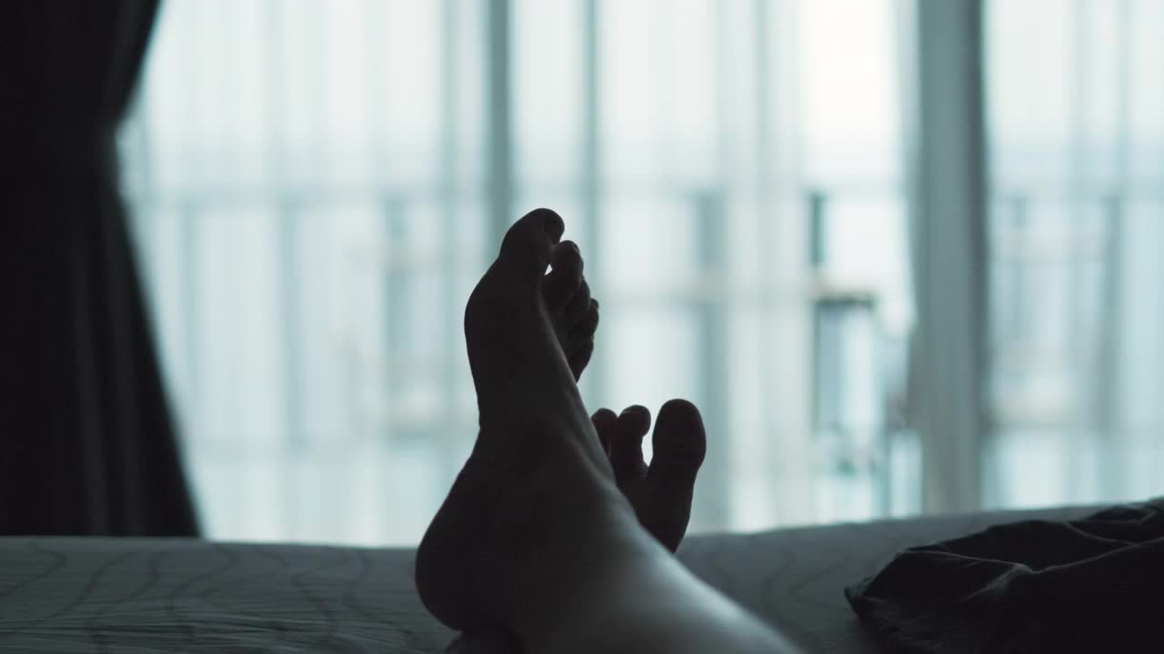 一个放松的女人躺在床上，交叉腿在毛毯上，在酒店度假胜地看风景视频下载