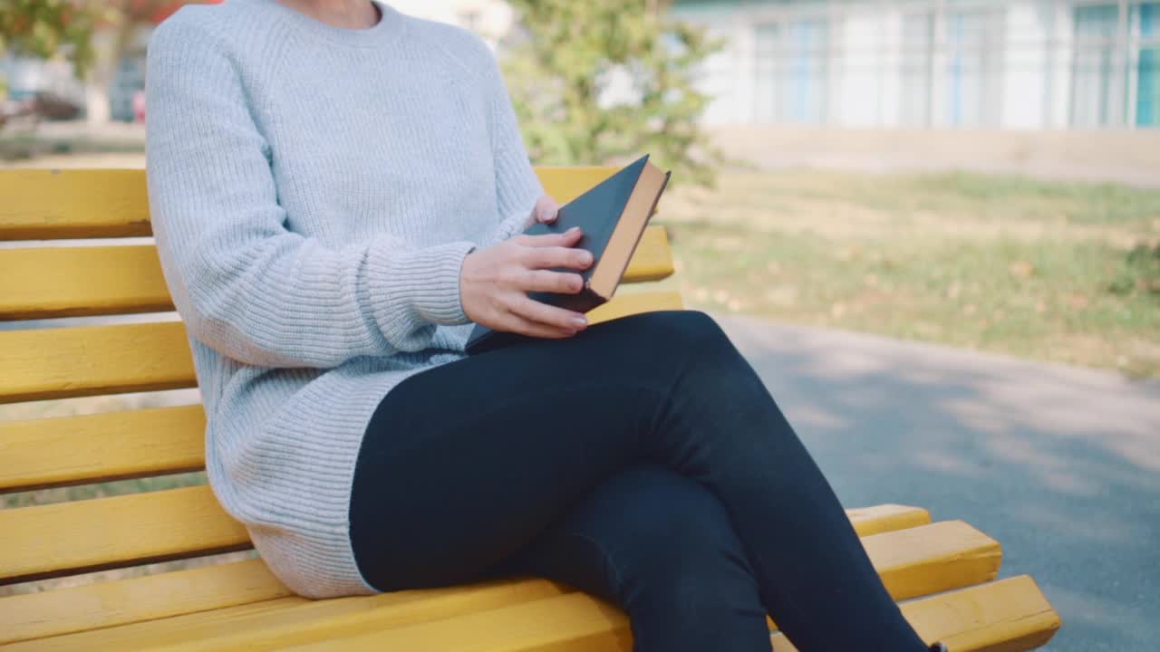 一个女孩手里拿着一本书坐在公园的长凳上。视频素材