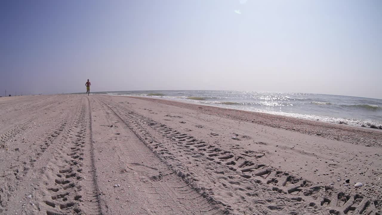 在阳光明媚的日子里，一名男子在沙滩上跑着接近摄像机视频素材