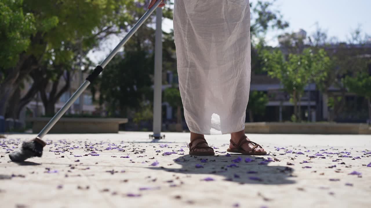 一个陌生的女人在城市广场上扫落下来的花瓣。年轻的白人女士清洁地板在地中海国家的阳光在慢动作。生活方式和性质。视频下载