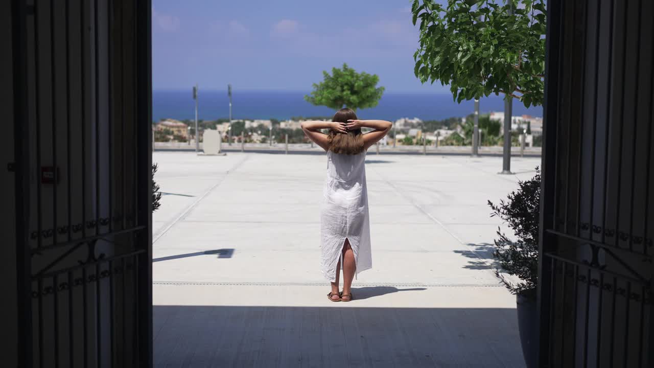 年轻女子站在阳光下欣赏美丽的地中海自然的夏季度假胜地。在阳光下休息的白人女性游客的背面。缓慢的运动。视频素材