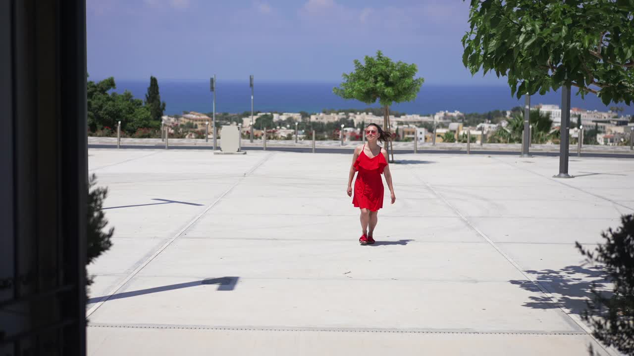 兴奋的年轻苗条的美丽的女人在地中海的夏季度假胜地，穿着红色的裙子和太阳镜跑步旋转。广角拍摄的快乐游客享受假期。缓慢的运动。视频素材