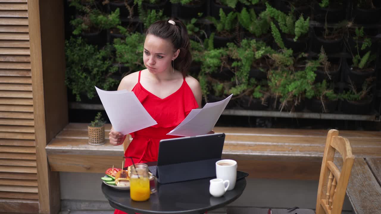 前视图问题集中的女人分析文件在平板键盘上打字，在假期在线工作。专业专注的白人自由职业者在户外咖啡馆。视频素材