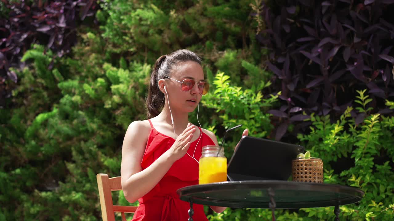 来自阳光明媚的地中海国家的一名年轻白人女子正在用平板电脑进行远程视频聊天。照片中自信美丽的自由职业者交谈和打手势讨论业务。视频素材