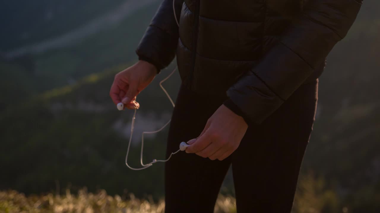愉悦的女徒步者站在山顶俯瞰山谷，戴上耳机视频下载