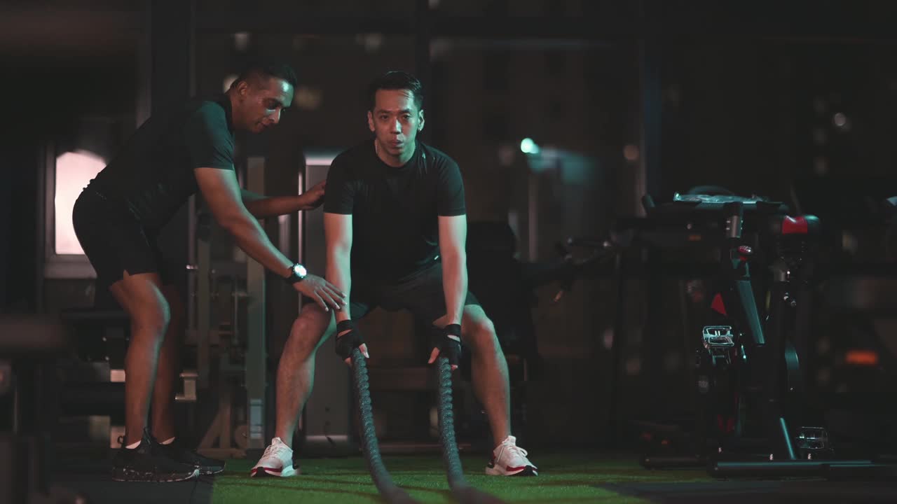 亚洲印度私人教练鼓励亚洲华人中成年人在健身房练习有挑战性的战斗绳视频素材