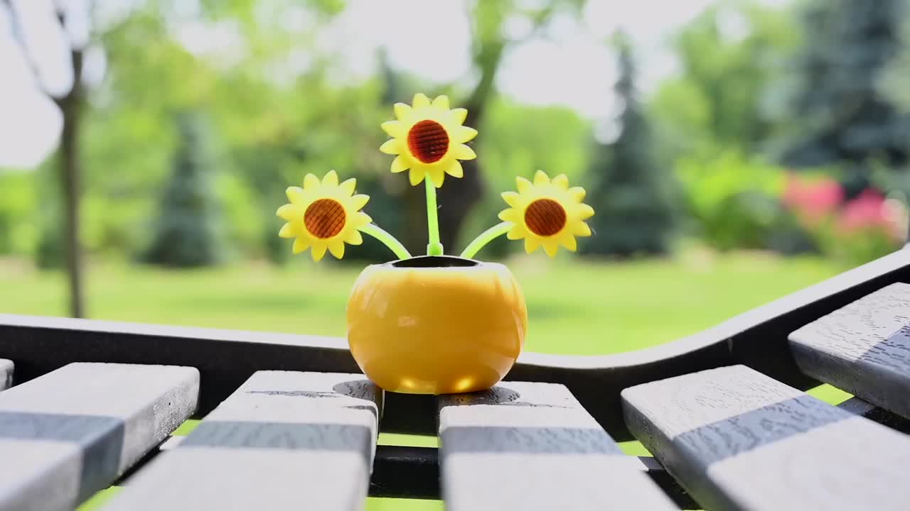 在花园的长椅上，一个由太阳能驱动的塑料人造向日葵在阳光下移动，代表可再生能源。视频素材
