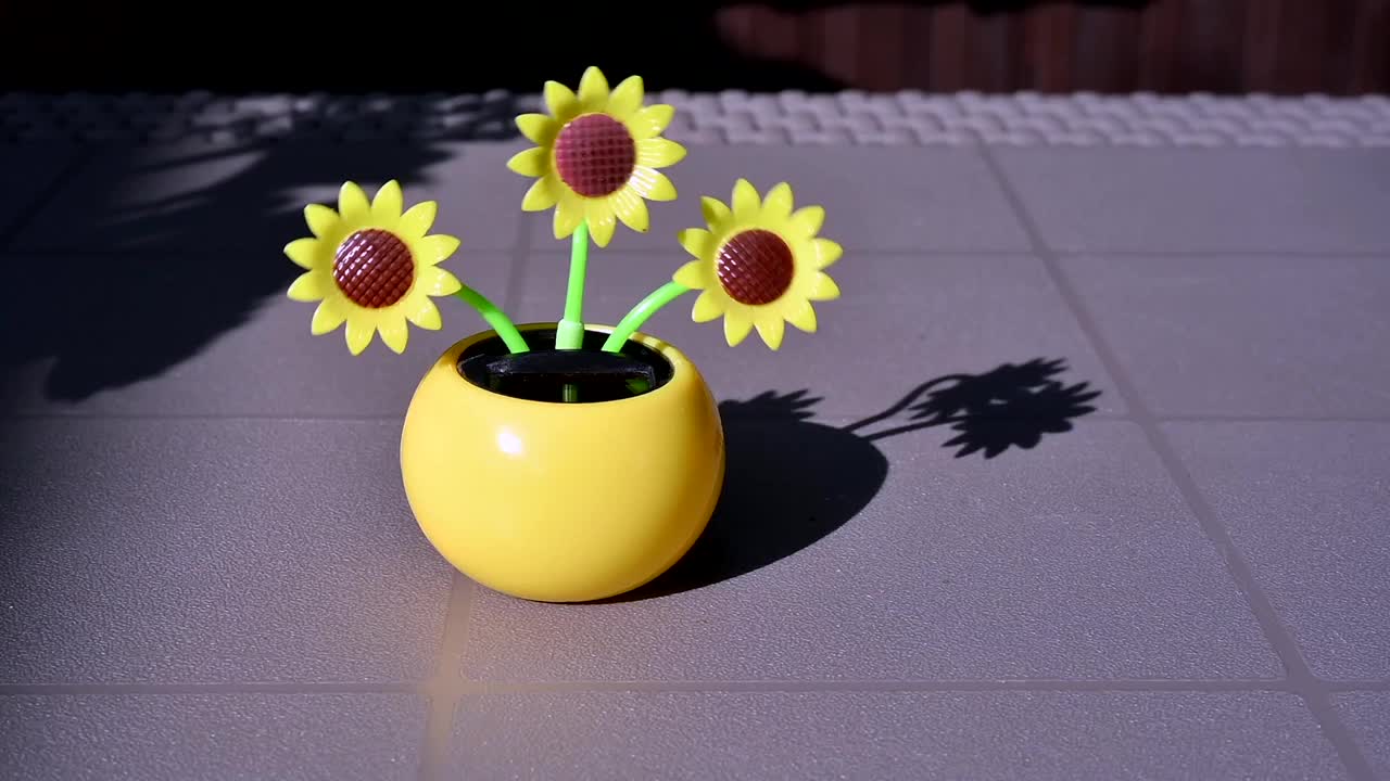 在花园的桌子上，一个由太阳能驱动的塑料人造向日葵在阳光下移动，代表可再生能源。视频素材