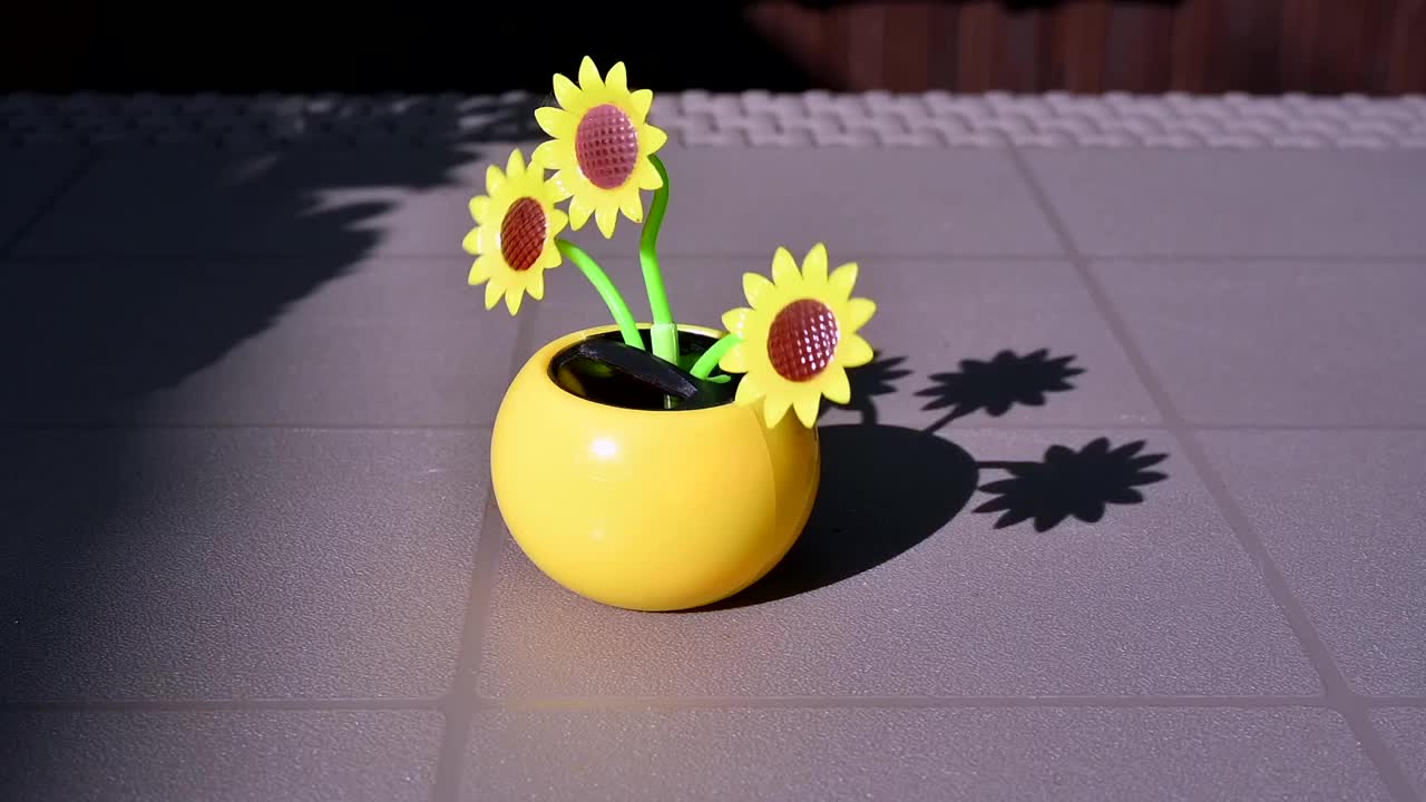 在花园的桌子上，一个由太阳能驱动的塑料人造向日葵在阳光下移动，代表可再生能源。视频素材