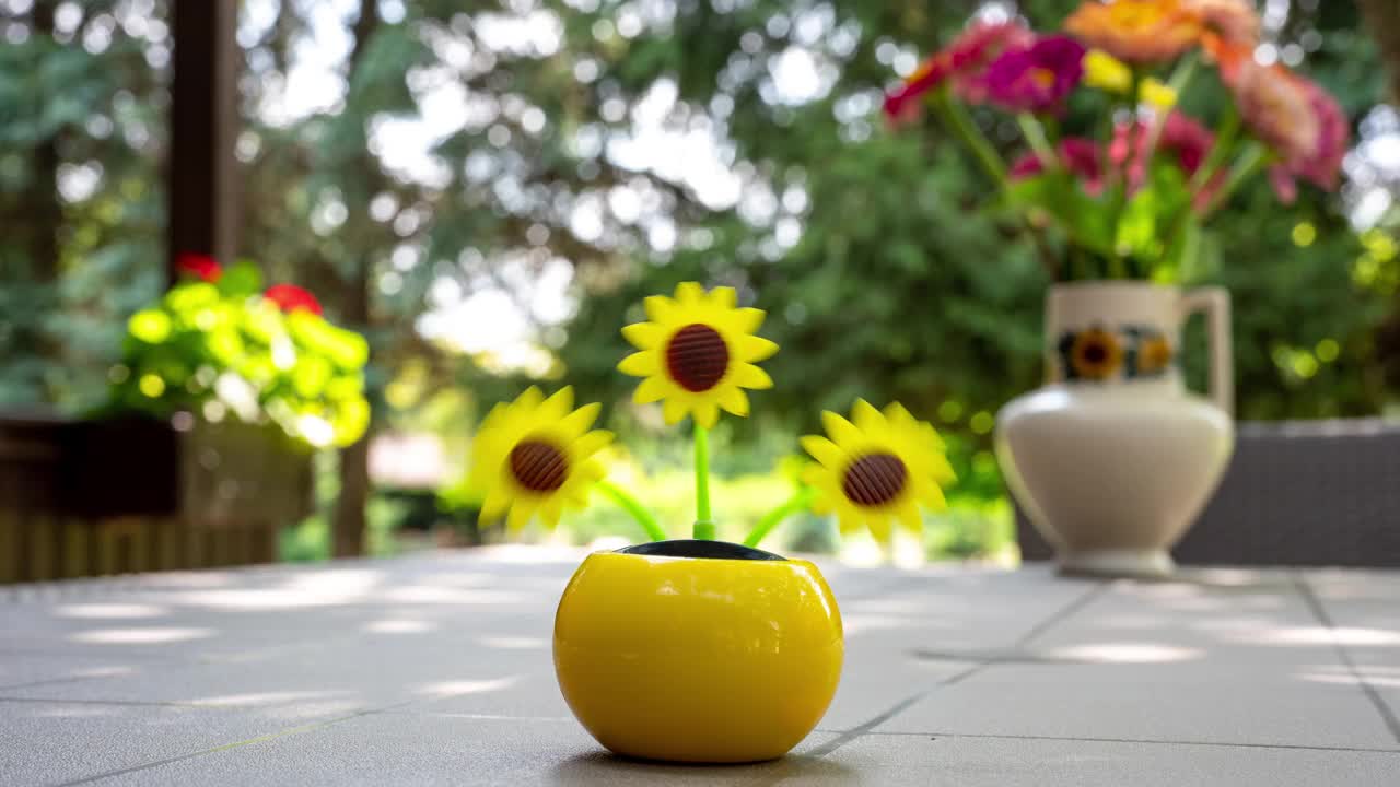 在花园的桌子上，一个由太阳能驱动的塑料人造向日葵在阳光下移动，代表着可再生能源。视频素材