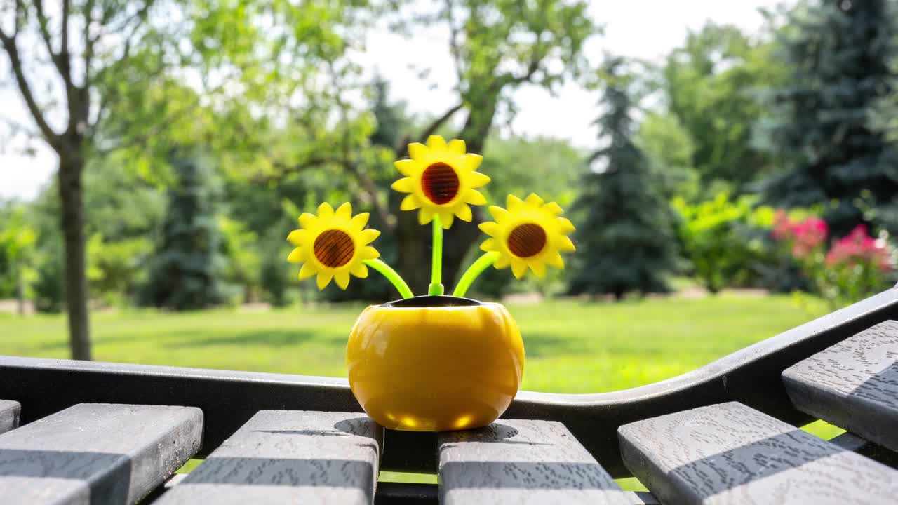 在花园的长椅上，一棵由太阳能驱动的塑料人造向日葵在阳光下移动，代表着可再生能源。视频素材