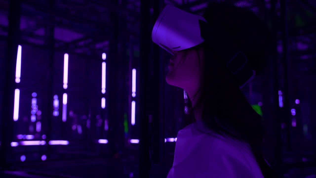 一个亚洲少女戴着虚拟现实头盔，在黑暗的夜晚，在五颜六色的紫外线照明下触摸空气。虚拟现实，可视化5G概念。视频下载