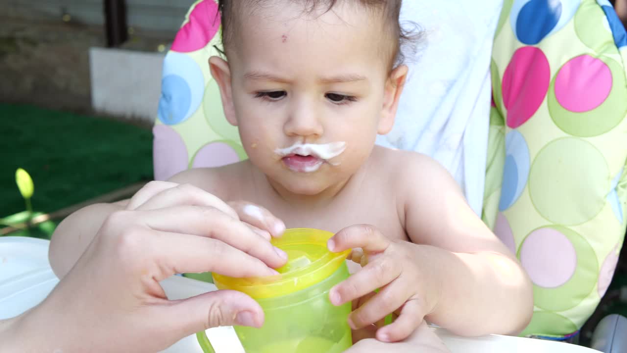 一个小男孩坐在儿童椅上的肖像。快乐的孩子喝牛奶，开菲尔或奶制品从杯子。正确和天然的儿童营养视频素材