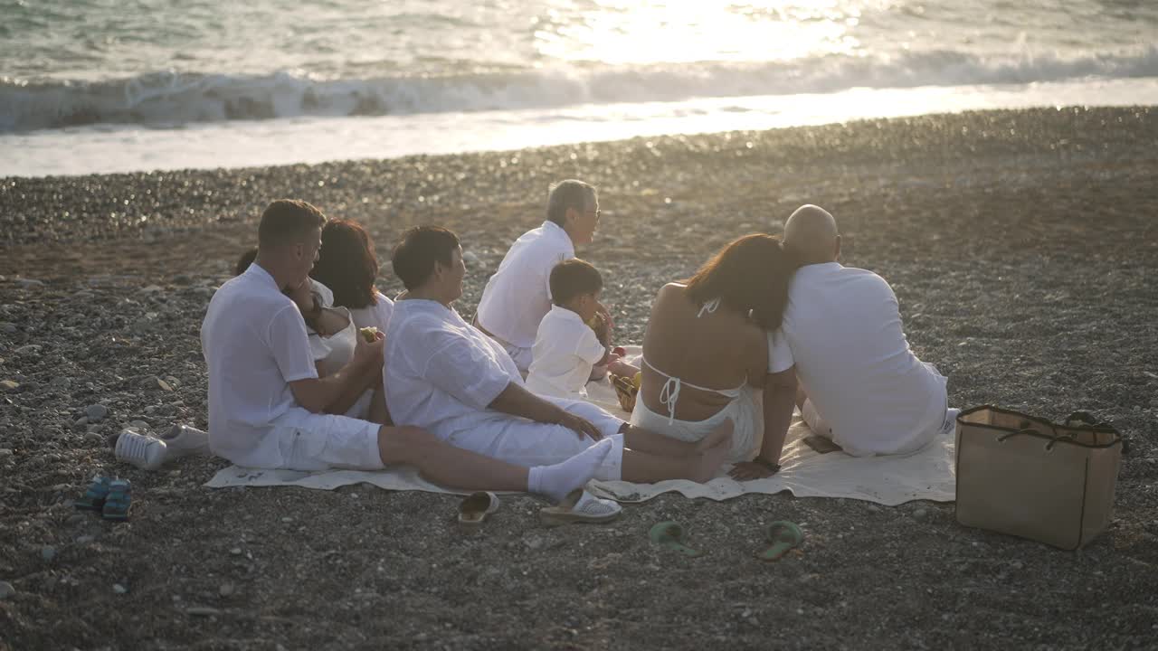 悠闲的亚洲家庭欣赏地中海海岸的日落与泡沫飞溅的海浪在背景与阳光反射在水中。旅游休闲理念。视频素材