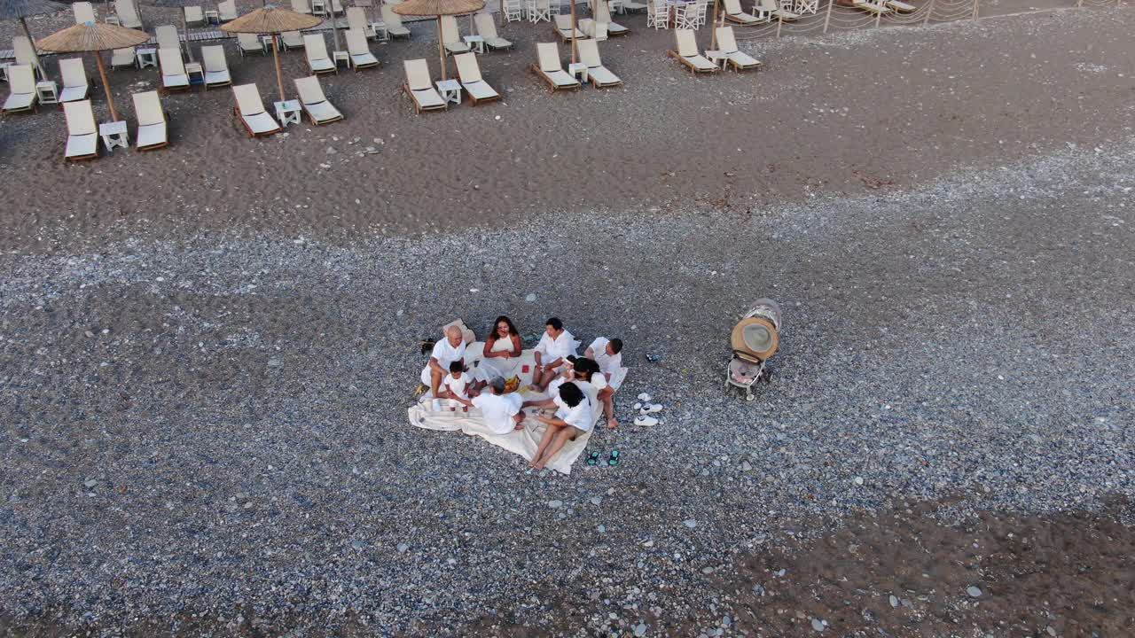 广角鸟瞰图，快乐的亚洲家庭坐在旅游胜地的岩石海滩谈笑风生。快乐的男人，女人和孩子在国外的地中海国家享受假期。视频下载
