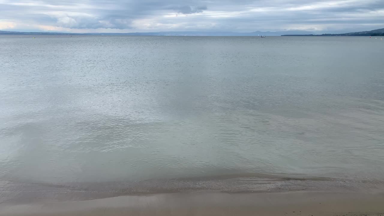 多云的天空，沙滩和平静的湖水在日内瓦湖上视频素材