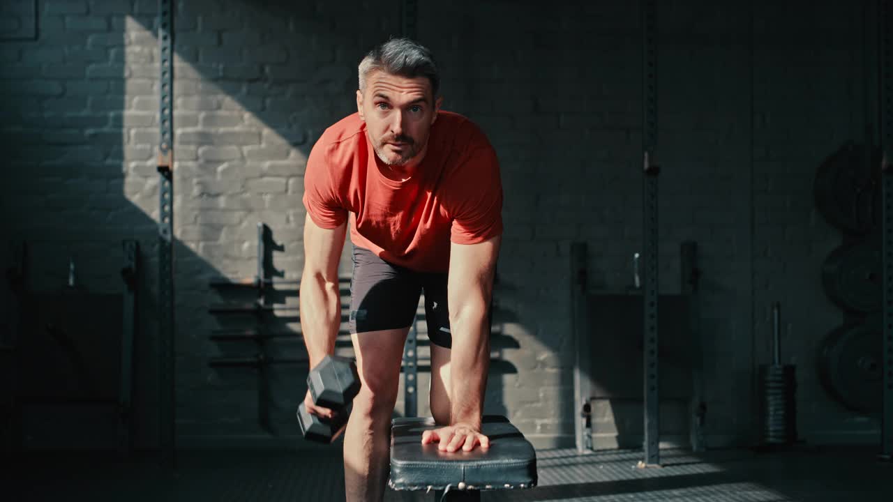 一个英俊的成熟男人在健身房里用哑铃锻炼的4k视频片段视频下载
