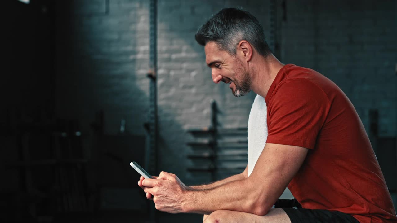 4k视频记录了一个英俊成熟的男人在健身后独自坐在健身房使用手机视频下载