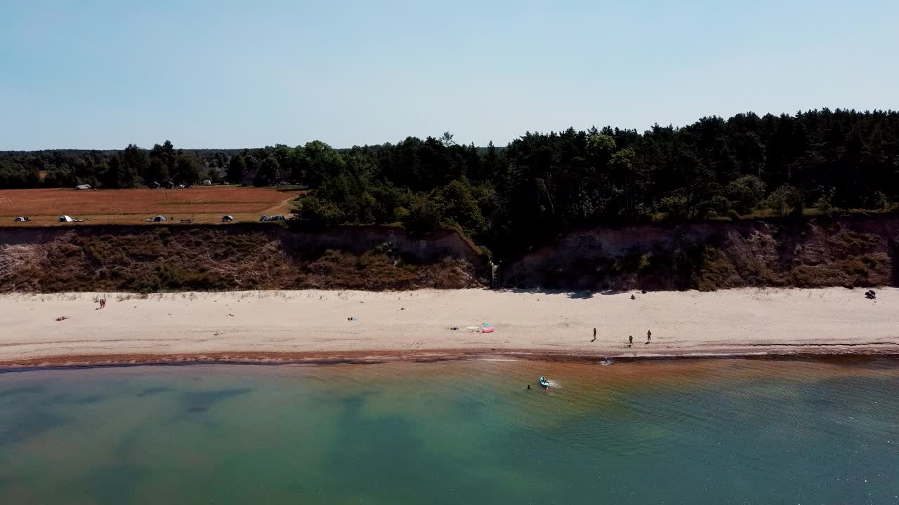 飞越海岸线波罗的海Jurkalne海滨悬崖附近的Pavilosta拉脱维亚和山体滑坡与杂草丛生，波纹洞点缀悬崖和鹅卵石。空中Dron视图。阳光明媚的夏天视频素材