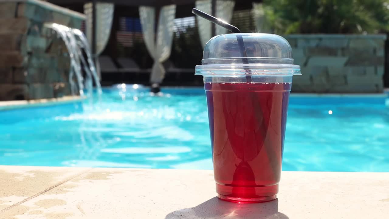 泳池边用吸管一次性塑料杯盛着鲜红色的酒精鸡尾酒视频下载