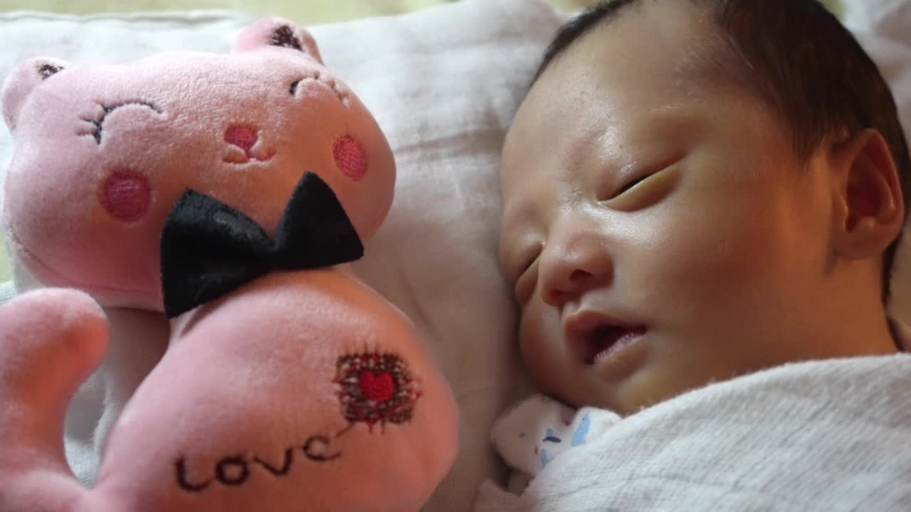 睡意朦胧的新生男婴和他的粉色猫咪毛绒玩具视频下载