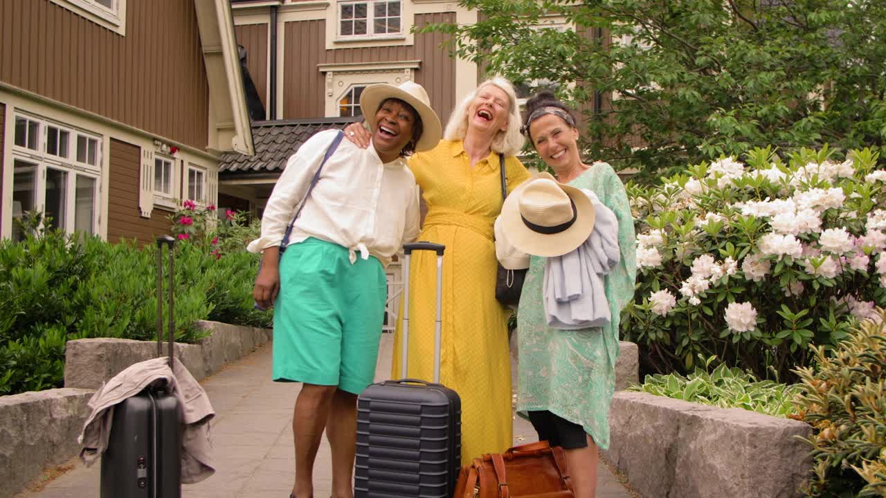 愉快的老年女性朋友们带着轮式行李在假期的人行道上散步视频素材