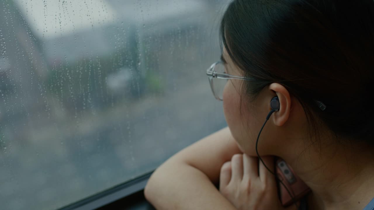 忧伤的女人坐在窗边看雨，听着音乐视频素材