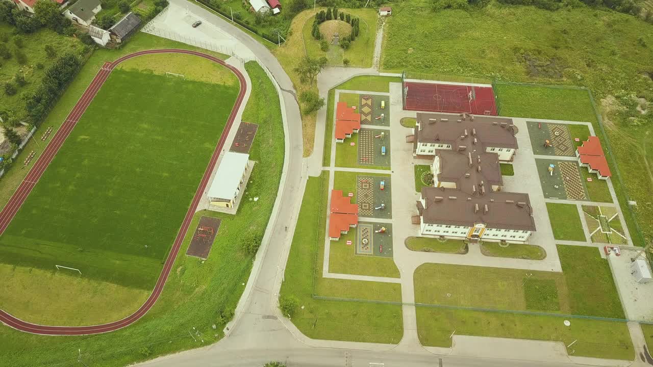 农村学校建筑附近的体育场鸟瞰图，红色的跑道和绿色的草地足球场。视频素材