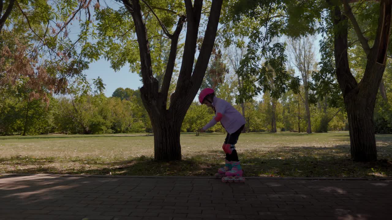 戴着粉色头盔的女孩学习轮滑公园跑道视频下载