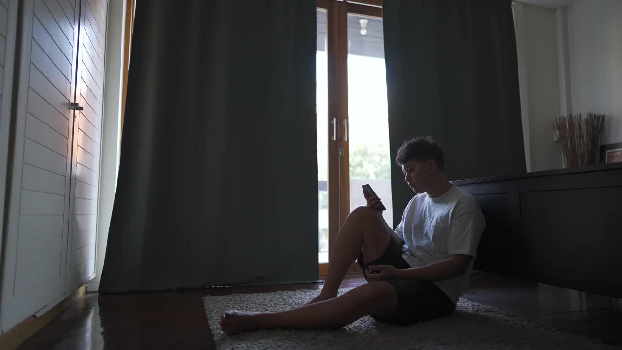 4K紧张的亚洲男人坐在卧室里用手机。视频素材