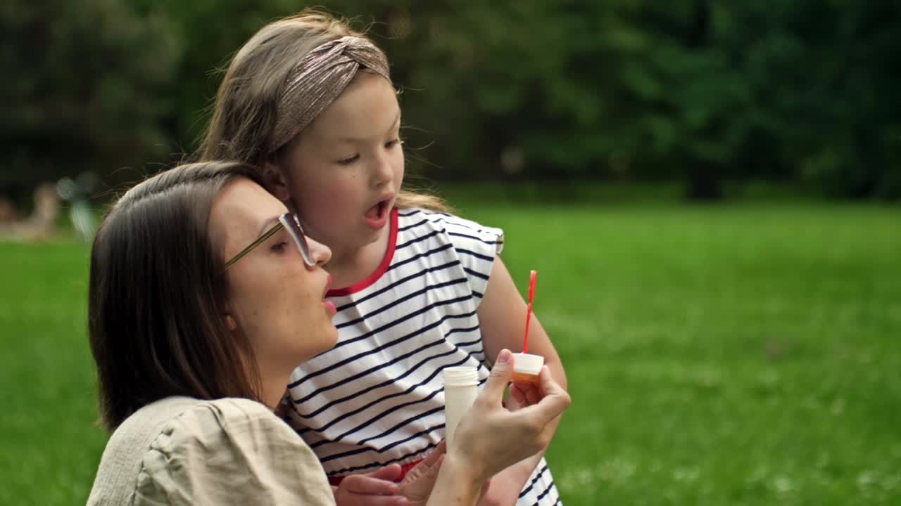 一个年轻的女人和她6岁的女儿正在吹彩虹泡泡。有趣的家庭度假视频素材