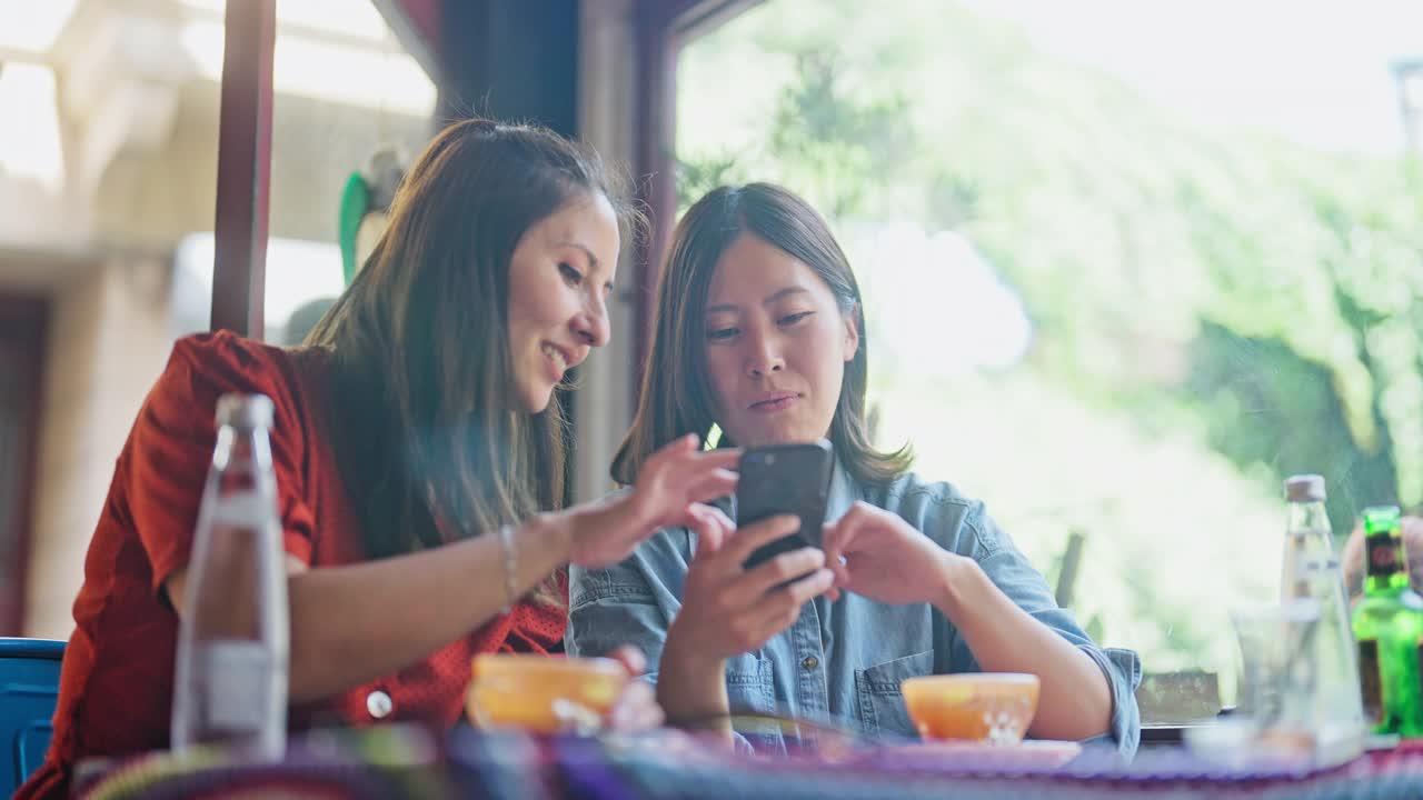 两个多民族的女性朋友在咖啡馆里一起玩手机视频下载
