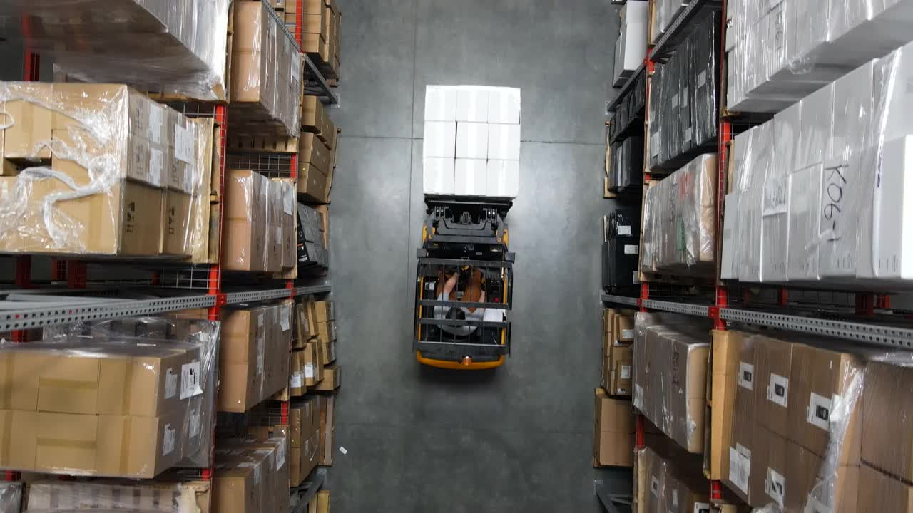 仓库工人在仓库内用叉车搬运货物托盘的架空小车跟踪拍摄视频下载