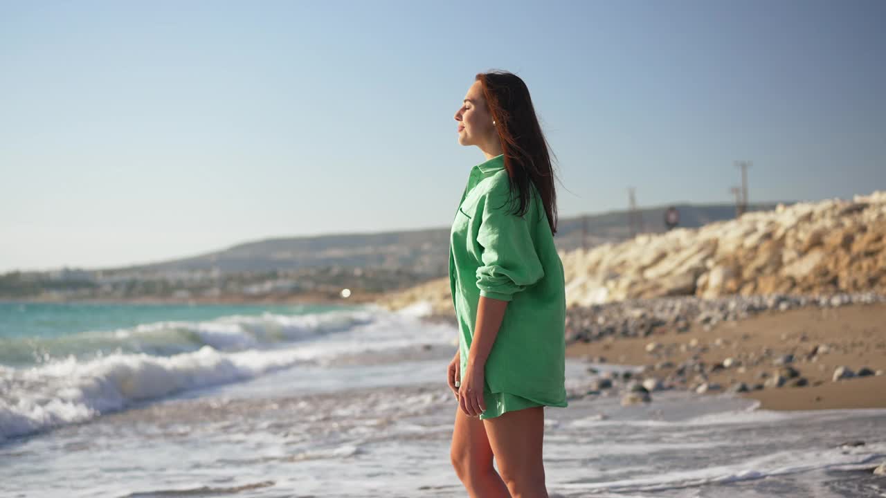 一边的快乐年轻女子吸入新鲜的空气举起双手欣赏美丽如画的地中海在沙滩上。美丽的白种人游客在阳光下享受休闲时光。视频素材