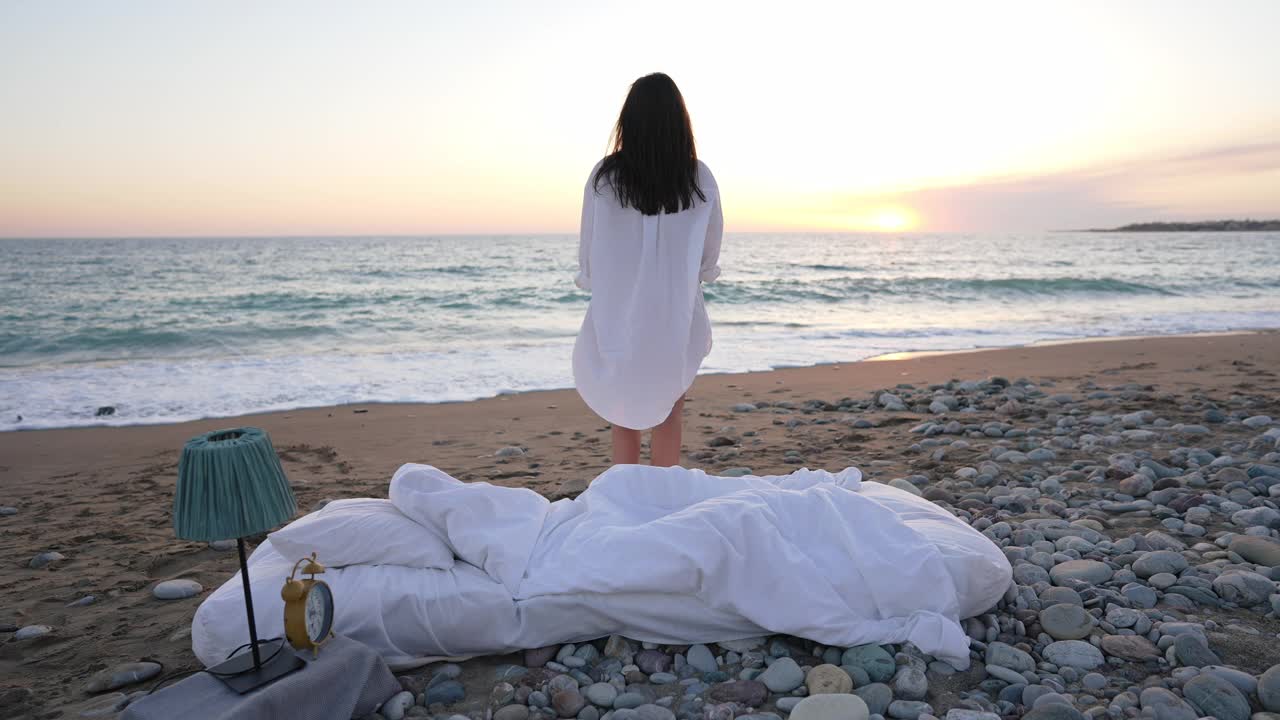 苗条的年轻白人妇女举起双手，伸展在风景如画的地中海风景，白色的床躺在前面的沙子。快乐无忧无虑的女士在户外欣赏日出。视频素材