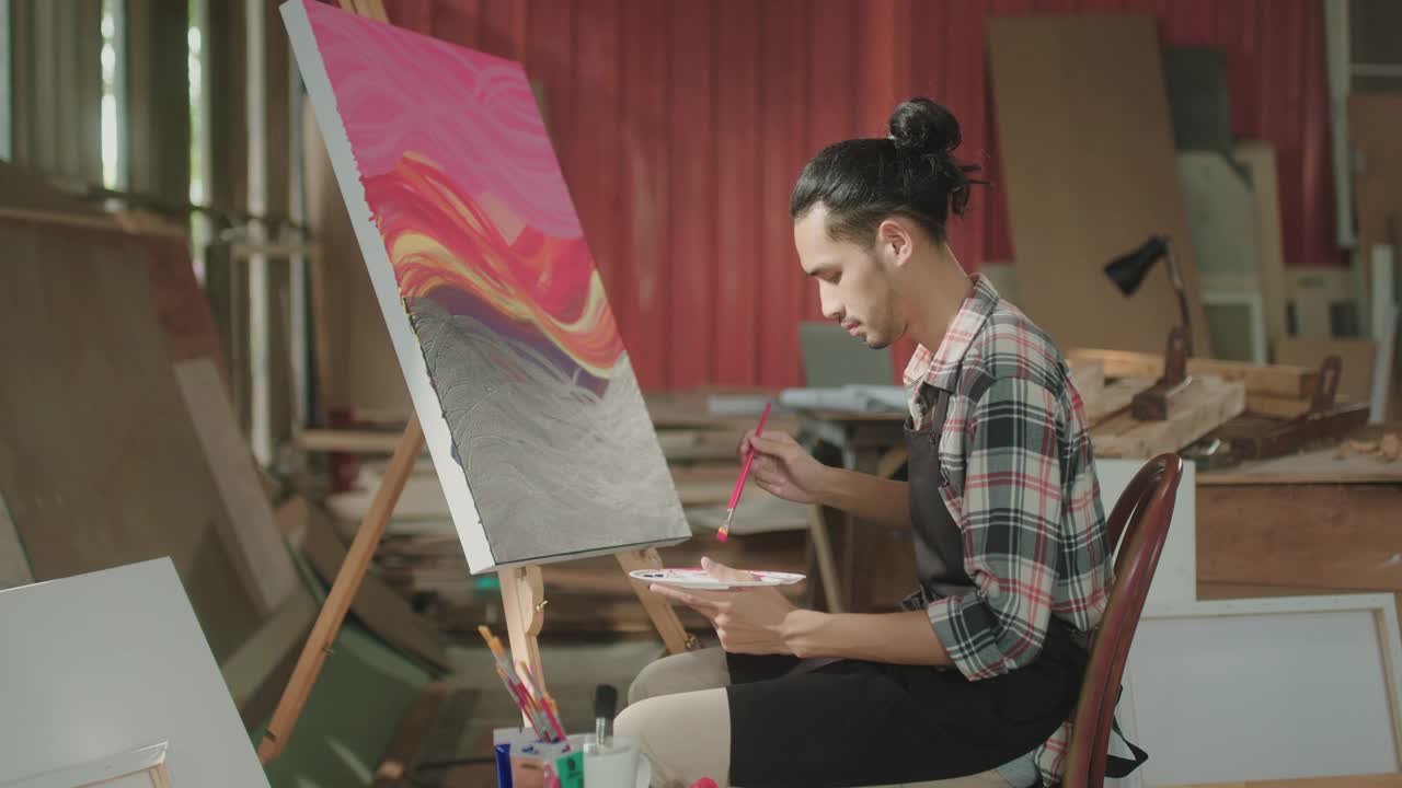 年轻的亚洲男性艺术家在工作室里用丙烯颜料在帆布上作画视频下载