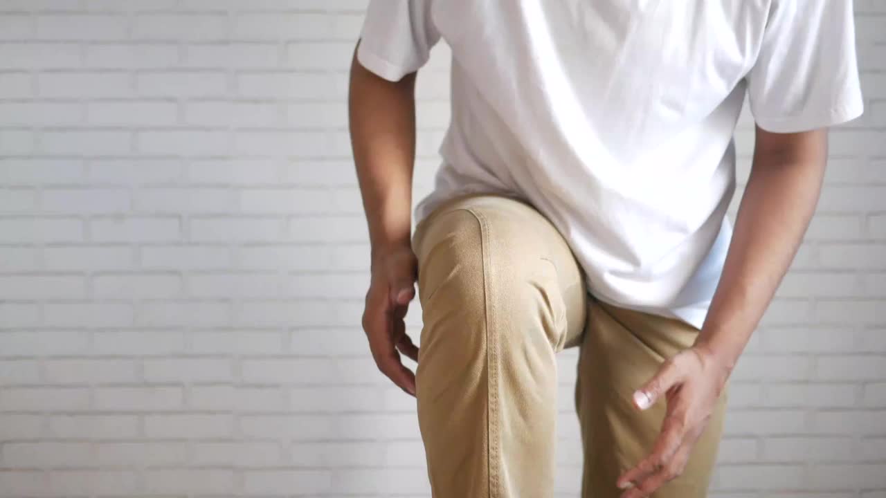 男人忍受着膝盖关节疼痛，站在白色的墙壁上视频素材