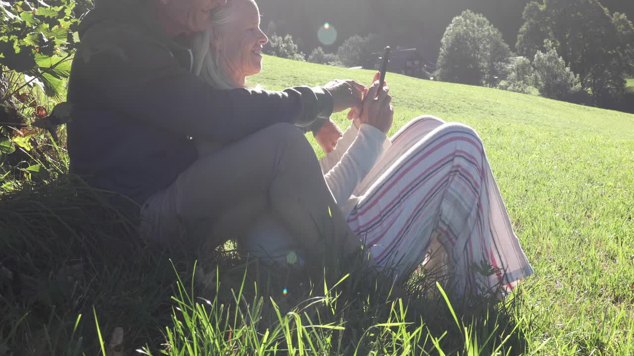 一对夫妇在山间草地上放松，看智能手机视频下载