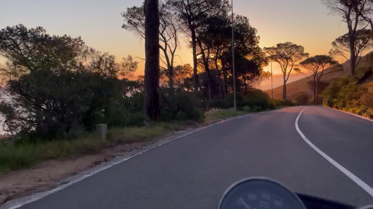 黄昏复古摩托车骑行，左侧为树木和海洋，右侧为上升山坡视频下载