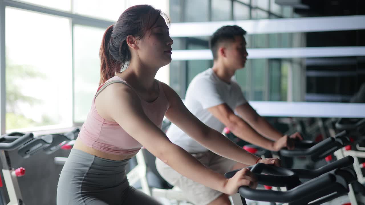 亚洲女人和男人在健身房进行自行车训练视频素材