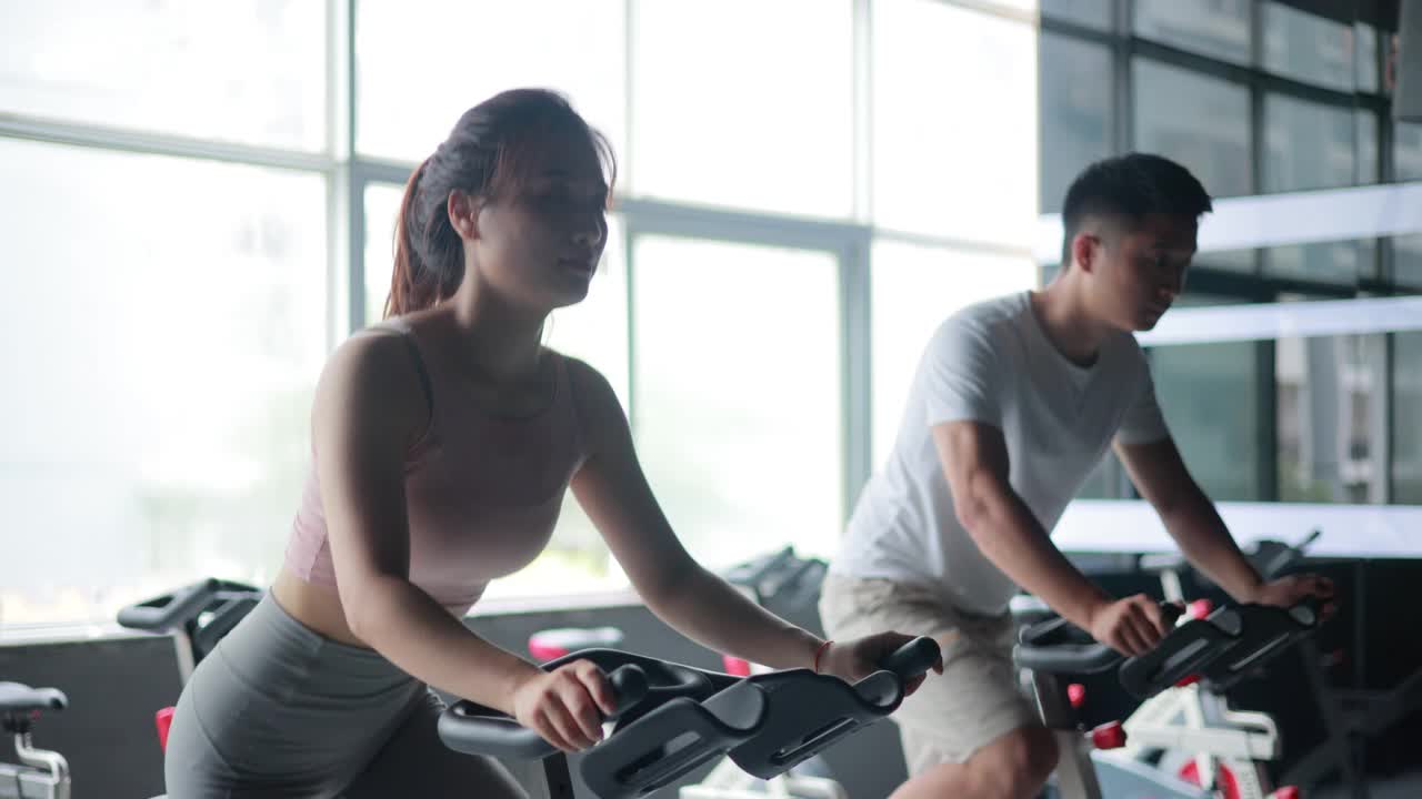 亚洲女人和男人在健身房进行自行车训练视频素材